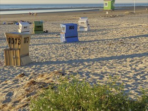 Scattered beach chairs on sand with sea in the background, people, small green hut, langeoog,