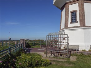 Partial view of a lighthouse with lattice and flowers, sea and blue sky in the background,