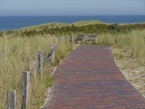 Paved path along the dunes with benches and a view of the sea under a clear sky, langeoog, germany