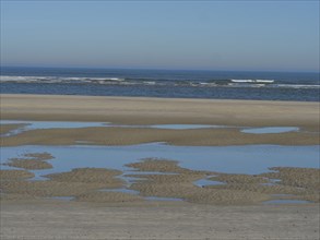 Quiet sandy beach with puddles of water and a view of the wide, calm sea, langeoog, germany