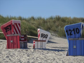 Close-up of colourful beach chairs in the sand with dunes in the background, langeoog, germany