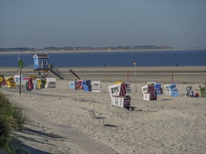 Colourful beach chairs stand on a wide sandy beach with a view of the calm sea, langeoog, germany