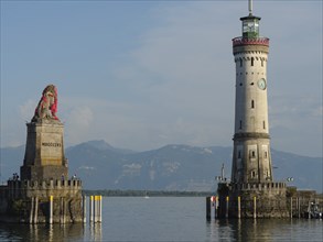 Lighthouse and lion statue at the entrance of a harbour, mountain landscape in the background,