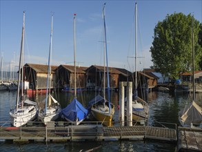 A quiet harbour with sailing boats in front of wooden huts, illuminated by the setting sun and calm