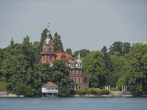 A castle with towers and red bricks, surrounded by trees on the lakeshore, Lindau, Lake Constance,