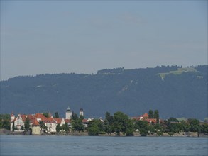 Small town with church towers against a background of mountains and a lake in the foreground,