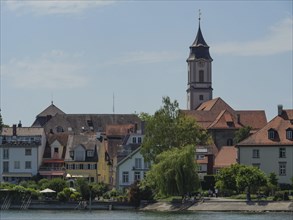 Church with a high tower surrounded by houses and trees in a lakeside village, Lindau, Lake