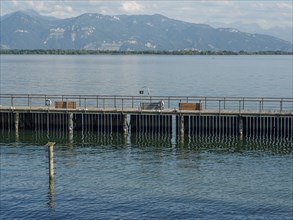 A wooden jetty on the lakeshore with benches and a view of the mountains, Lindau, Bavaria, Germany,