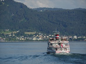 A ship sails on the lake towards a town surrounded by mountains, Lindau, Bavaria, Germany, Europe