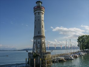 Lighthouse next to boats on the lakeshore with clear sky and summer atmosphere, Lindau, Bavaria,