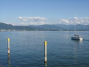 View of a lake with a sailing boat and mountains in the background on a calm day, Lindau, Bavaria,