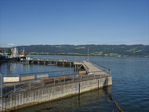 Harbour with a jetty and calm water, wooden railings on the jetty and a natural backdrop of