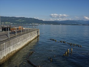 Calm lake with a wooden pier, mountains and clouds in the background, Lindau, Bavaria, Germany,