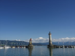 A lighthouse and a statue flanked by boats in the harbour on a clear day, Lindau, Bavaria, Germany,