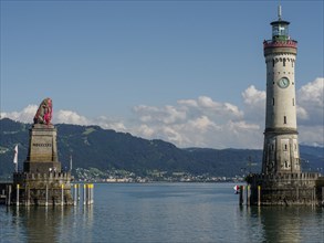 A lighthouse and a lion statue on the lakeshore with mountains in the background, Lindau, Bavaria,