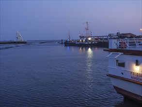 Boats lie quietly in the harbour, the twilight gives the water and sky a blue hue, lights shimmer