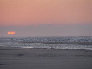 The sun disappears behind the sea on the horizon and colours the sky orange, juist, east frisia,