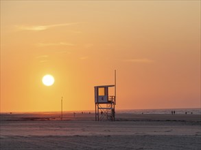 A rescue tower stands on the beach, the sky is coloured orange by a breathtaking sunset, juist,