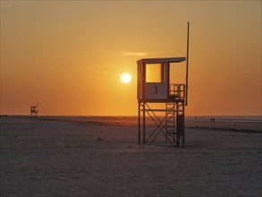 Beach at sunset with a rescue tower and calm, orange-coloured atmosphere, juist, east frisia,