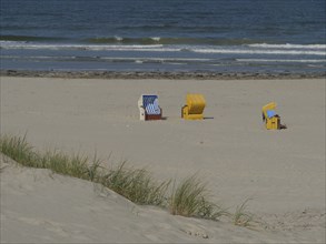 Two empty beach chairs on the beach, dune grass in the foreground and the blue sea in the