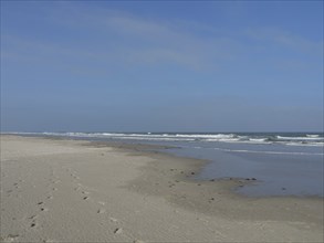 Extensive beach with waves and footprints in the sand under a blue sky, juist, east frisia,