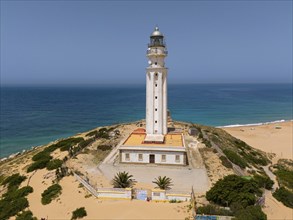 White lighthouse on the coast with a view of the sea and the beach under a clear sky, aerial view,