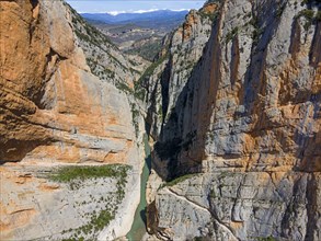 An aerial view of a narrow gorge with steep rock faces and a river flowing through the valley,