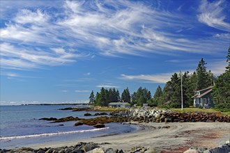 A quiet beach with blue sky, white clouds, sea, sand, rocks, trees and few houses on the coast,