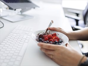 Food at work: A woman/man holds a bowl of muesli with fruit at her desk in Berlin, 25/07/2024