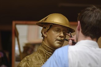 A make-up artist applies gold paint to an actor's face before a performance