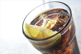 Part of a drinking glass with fresh cola, ice cubes and lemon slice, refreshing sweet caffeine