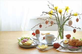 Easter breakfast served on a wooden table with a bouquet from daffodil flowers, spring branches and