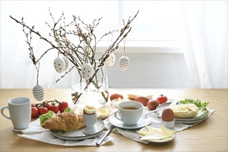 Breakfast with Easter egg decoration on a wooden dining table, place setting on a spring holiday,