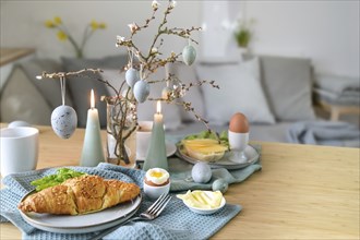 Breakfast table with boiled egg, croissant and pastel turquoise Easter decoration in a small living