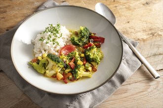 Vegetarian broccoli curry with rice and parsley garnish in a gray plate on a rustic wooden table,