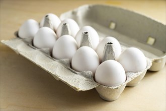 Ten fresh white eggs in a cardboard box on a wooden table, food and Easter concept, selected focus,