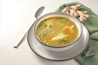 Homemade chicken soup with vegetables, ginger and parsley in a bowl, green napkin and spoon on a