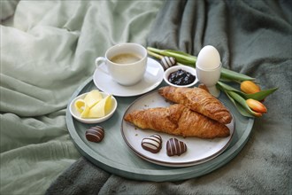 Breakfast served with love in bed, coffee, croissant, jam, egg, some chocolate hearts and tulips on