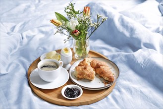 Happy morning with breakfast in bed, flowers, croissant, coffee and more on a tray on blue white