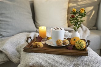 Hot chocolate drink with marshmallows and mini muffins on a tray with candle, flowers and autumn