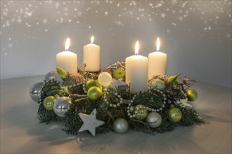 Fourth Advent, wreath with four burning white candles and green Christmas decoration on a table,