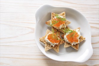 Canapes with red caviar on toasted bread in star shape with cream and dill garnish on a white