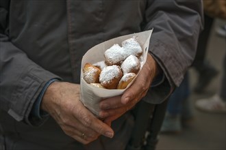 Man holding a paper bag of Mutzenmandeln, deep fried shortcrust dough pastry with almonds covered