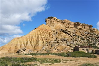 Small hut in front of a striking rocky hill in a desert-like landscape under a blue sky, Bardenas