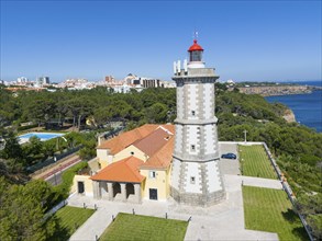 A lighthouse with a red top next to a building with a view of the forest and the sea, aerial view,