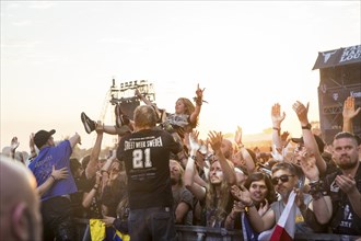 Crowdsurfers in front of the evening sun at the Wacken Open Air in Wacken. The traditional metal