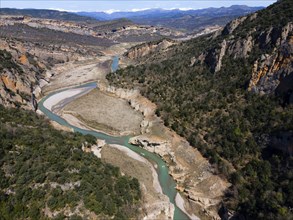 An aerial view of a deep gorge with a green river surrounded by steep, wooded cliffs, aerial view,