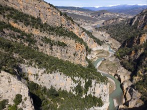 A dry river course winds through a deep gorge in a mountainous and wooded environment, aerial view,