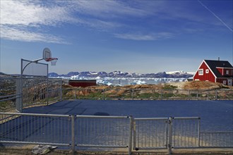 A basketball court on a coastline with a red house in the background and icebergs in the ocean,