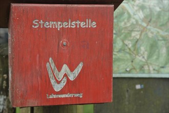 Red stamping point with hiking sign on the Lahnwanderweg trail at the source of the Lahn with